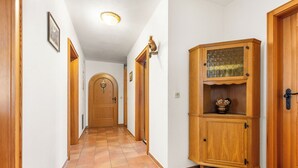 Um corredor com portas de madeira, chão de azulejos e um armário de madeira com portas de vidro.