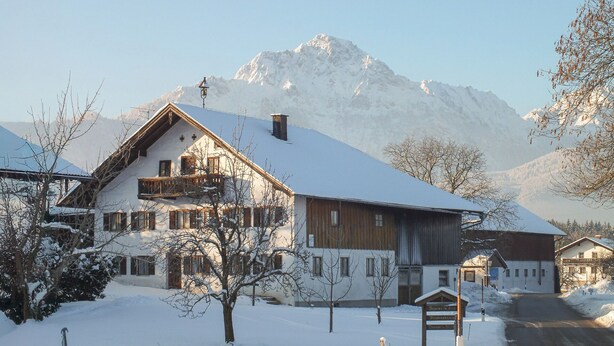 Uma aldeia montanhosa coberta de neve, com casas de madeira tradicionais e vista clara das montanhas.