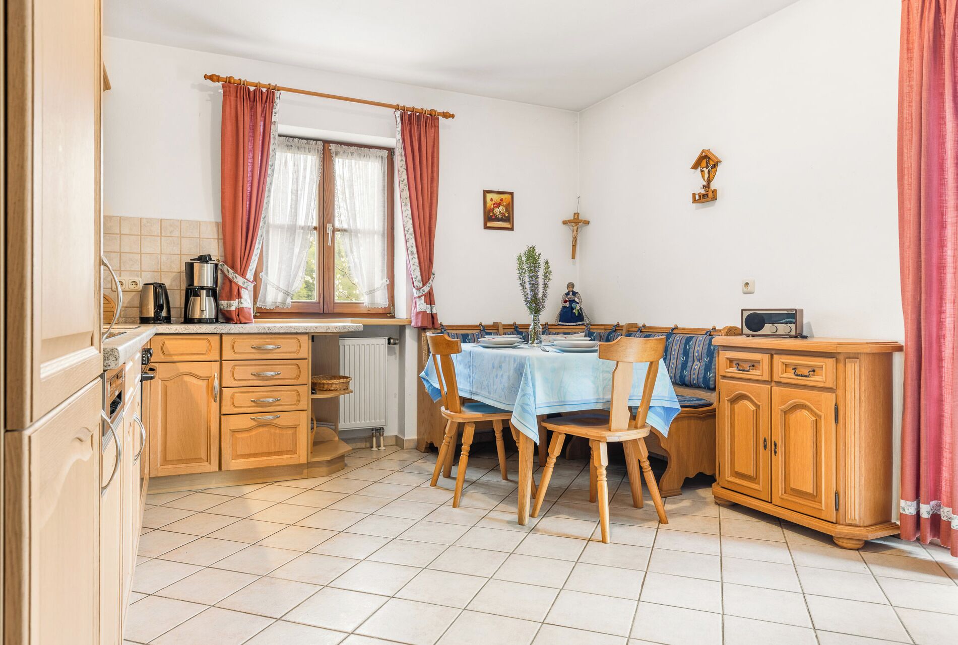 Eine Küche mit Holzausstattung, einem Esstisch mit Stühlen, einem Heizkörper und einem Fenster mit Vorhängen.