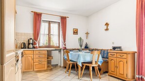 Uma cozinha com armários de madeira, uma mesa de jantar com cadeiras, um radiador e uma janela com cortinas.