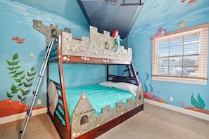 A bunk bed with a castle-themed design, a window with blinds, and a ceiling fan.