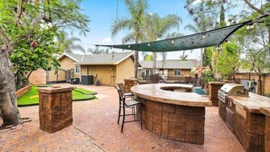 An outdoor patio area with a stone barbecue station, seating, and a small pool.
