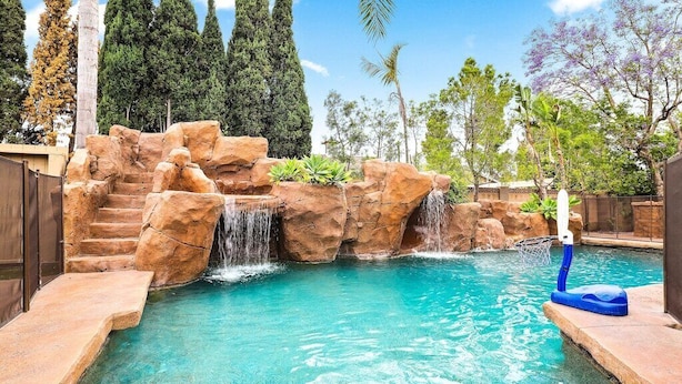A swimming pool with a waterfall feature, surrounded by rock formations and plants.