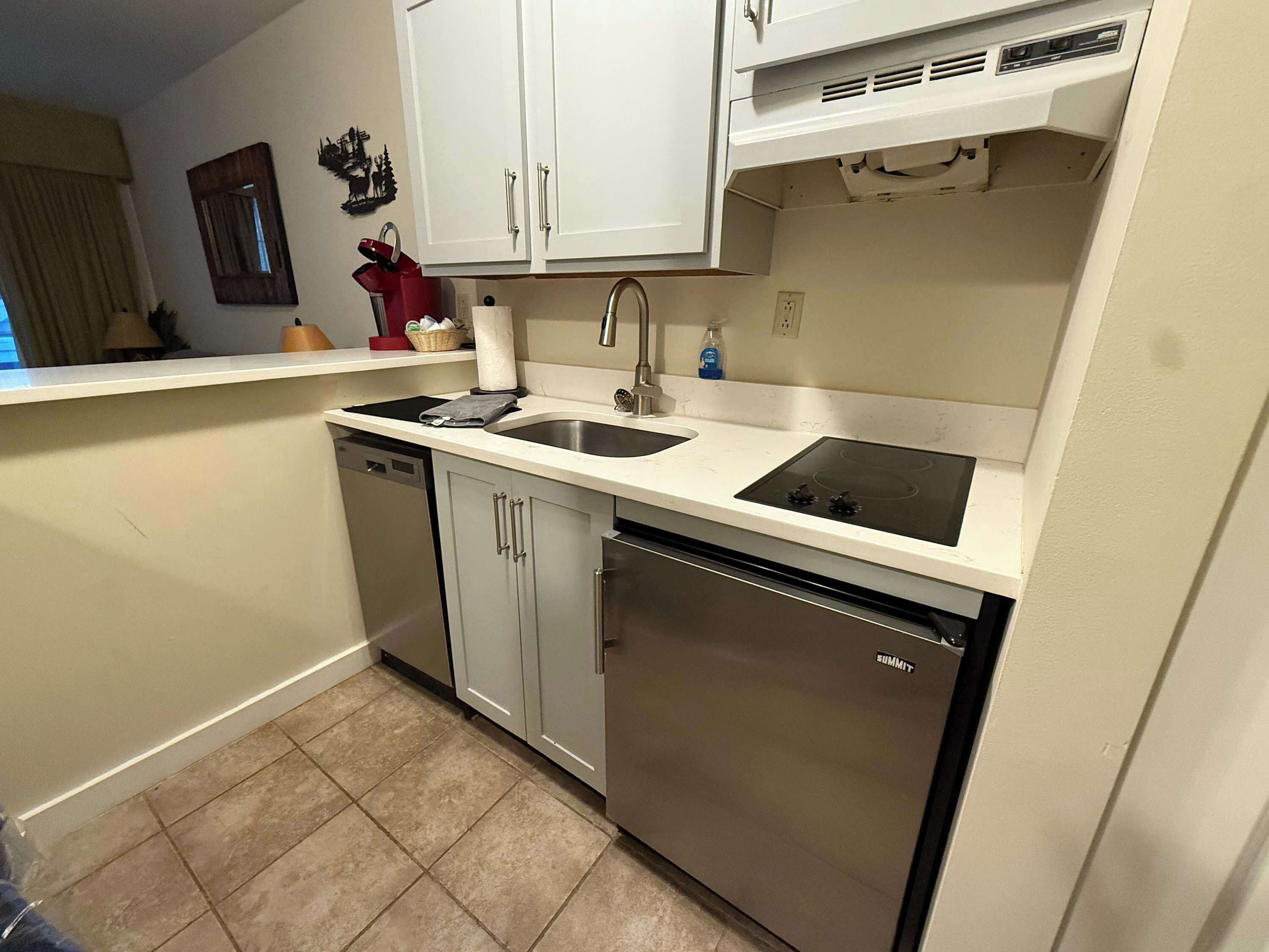 A compact kitchen with white cabinets, a stainless steel dishwasher, and a built-in oven.