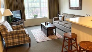 Una sala de estar con un sofá, una mesa de centro, un televisor y una ventana con cortinas.