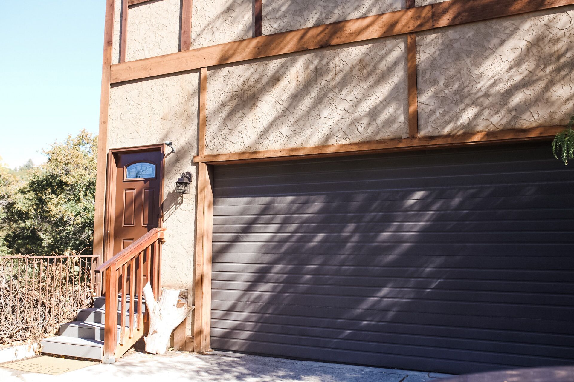 Un bâtiment doté d’un escalier en bois menant à une porte, à une porte de garage et à une boîte aux lettres.