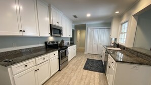 Una cocina moderna con armarios blancos, encimeras de granito, electrodomésticos de acero inoxidable y suelo de madera.