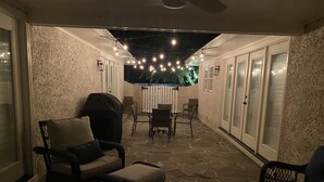 Un patio cubierto con suelo de piedra, mobiliario de mimbre e iluminación de guirnaldas.