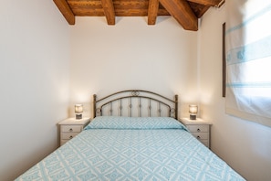 Ein Schlafzimmer mit einem Bett, zwei Nachttischen mit Lampen, einer Holzbalkendecke und einer Wand mit Vorhängen.