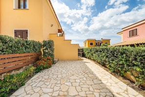 Ein Innenhof mit Steinpflasterung, einer Holzbank und einer Hecke mit roten Blüten.