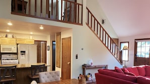 A spacious living area with a wooden dining table, red sofa, and a staircase leading to an upper level. - Treehouse Lodge- A quiet hilltop creative retreat, minutes from the lake. (Lake Arrowhead)