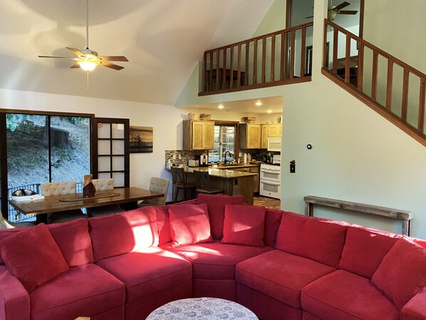 A spacious living area with a red sectional sofa, a dining table, and a kitchen in the background.