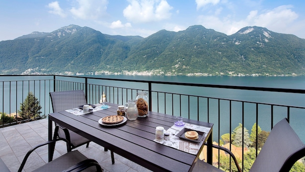 Un balcón con una mesa dispuesta para una comida, con vistas a un lago y montañas.