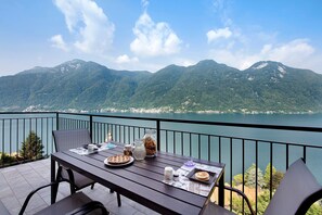 Un balcon avec une table dressée pour un repas, offrant une vue sur un lac et des montagnes.