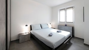 Un dormitorio moderno con cama, mesitas de noche, lámpara de pared e iluminación empotrada.