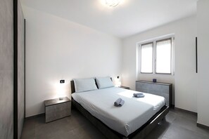 Ein modernes Schlafzimmer mit Bett, Nachttischen, Fenster und einer Wandleuchte.