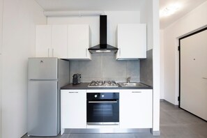 A compact kitchen with white cabinets, a stainless steel refrigerator, a built-in oven, and a black range hood.