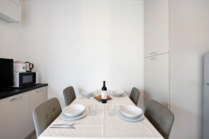A dining table set with plates, glasses, and a bottle of wine, with chairs around it. - Appartamento 4 Il Tornante with Lake & Mountain Views, Wi-Fi, A/C & Balcony (Nesso)