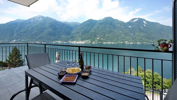 Un balcon avec une table dressée pour le dîner, offrant une vue sur un lac et des montagnes.