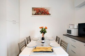 Uma área de jantar com uma mesa posta para dois, uma garrafa de champanhe e um buquê de flores.