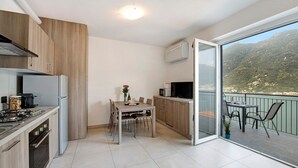 A modern kitchen with a dining area, a balcony with a view of mountains, and a sliding glass door. - Appartamento "7 Il Tornante" with Lake & Mountain Views, Wi-Fi, A/C & Balcony (Nesso)