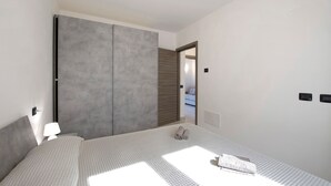 A bedroom with a bed, a nightstand, a lamp, a wardrobe, and a door leading to another room. - Appartamento "7 Il Tornante" with Lake & Mountain Views, Wi-Fi, A/C & Balcony (Nesso)