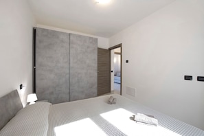 Une chambre à coucher comprenant un lit, une table de chevet, une lampe, une armoire et une porte donnant sur une autre pièce.