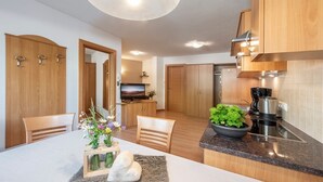 Una cocina moderna con armarios de madera, una zona de comedor con mesa y sillas, un televisor y una cafetera.