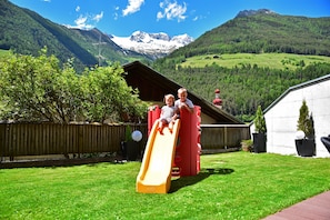 A playground with a slide, a wooden fence, and a mountain backdrop.