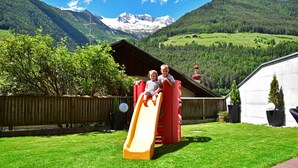 A playground with a slide, a wooden fence, and a mountain backdrop.