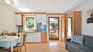 A compact kitchen with wooden cabinets, a dining table with chairs, a sofa, and a small dining area with a table and chairs.