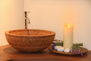 Una bacinella di legno con un rubinetto, una candela accesa e pietre decorative e lavanda.