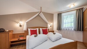 Een slaapkamer met een hemelbed, nachtkastjes, een kledingkast en een raam met gordijnen.