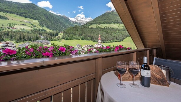 Een balkon met een tafel, twee wijnglazen en een fles wijn.