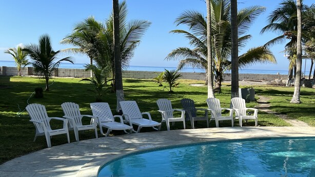 Une piscine bordée de chaises blanches et de palmiers, avec vue sur l’océan.