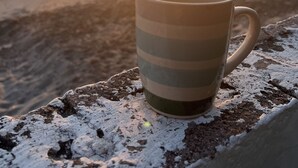 Une tasse posée sur une surface texturée, avec un coucher de soleil et l’océan en arrière-plan.