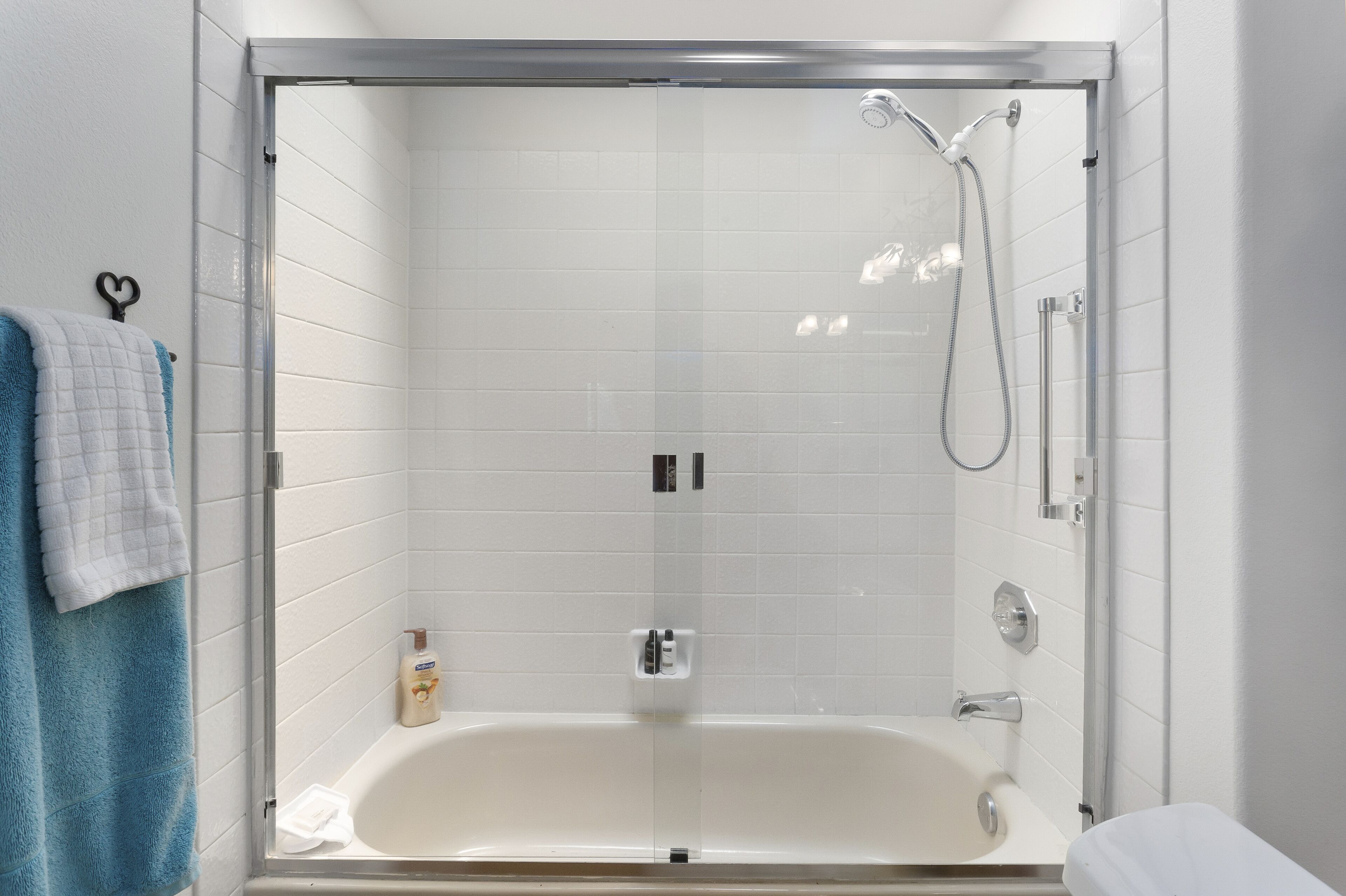 Une salle de bain moderne avec une douche à parois de verre, des murs recouverts de carreaux blancs et une baignoire blanche.