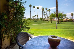 A patio with a round table and a decorative bowl, overlooking a well-manicured lawn and tall palm trees.
