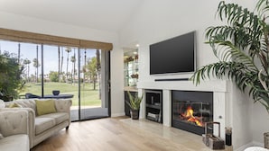 Ein Wohnzimmer mit Kamin, großem Fernseher und Blick auf einen Golfplatz.