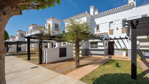 A courtyard with white buildings, a pergola, and a tree. - Townhouse overlooking golf course (La Torre Golf Resort)
