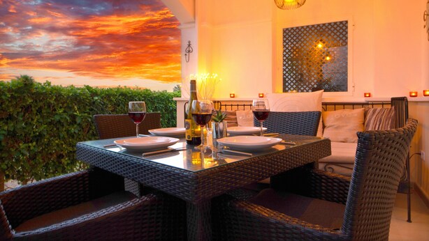 A dining area with wicker furniture, a table set for two, and a sunset mural on the wall. - Townhouse overlooking golf course (La Torre Golf Resort)