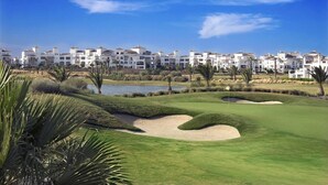 A golf course with sand bunkers, a pond, and a row of white buildings in the background. - Townhouse overlooking golf course (La Torre Golf Resort)