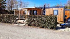 Une maison mobile en bois dotée d’un porche couvert, d’un petit garage attenant et d’une allée pavée.