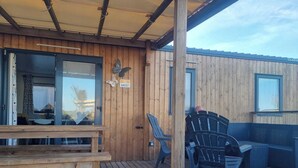Une terrasse en bois avec un banc et des chaises, une décoration en forme de papillon et un panneau indiquant le numéro M027.