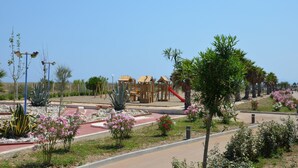Un terrain de jeux doté d’aires de jeux en bois et d’un toboggan rouge, entouré de jardins aménagés avec différentes plantes et fleurs.
