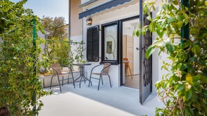 Une terrasse extérieure avec une table et des chaises, une porte donnant sur l’intérieur et de la verdure tout autour.