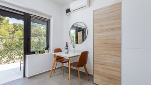 Un espace repas moderne avec une table blanche, deux chaises marron, un miroir rond et une fenêtre donnant sur un paysage verdoyant.