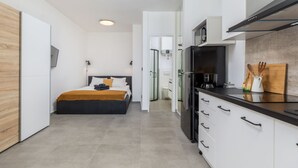 Une chambre d’hôtel moderne équipée d’un lit, d’une kitchenette et d’une salle de bain, visibles à travers une porte ouverte.