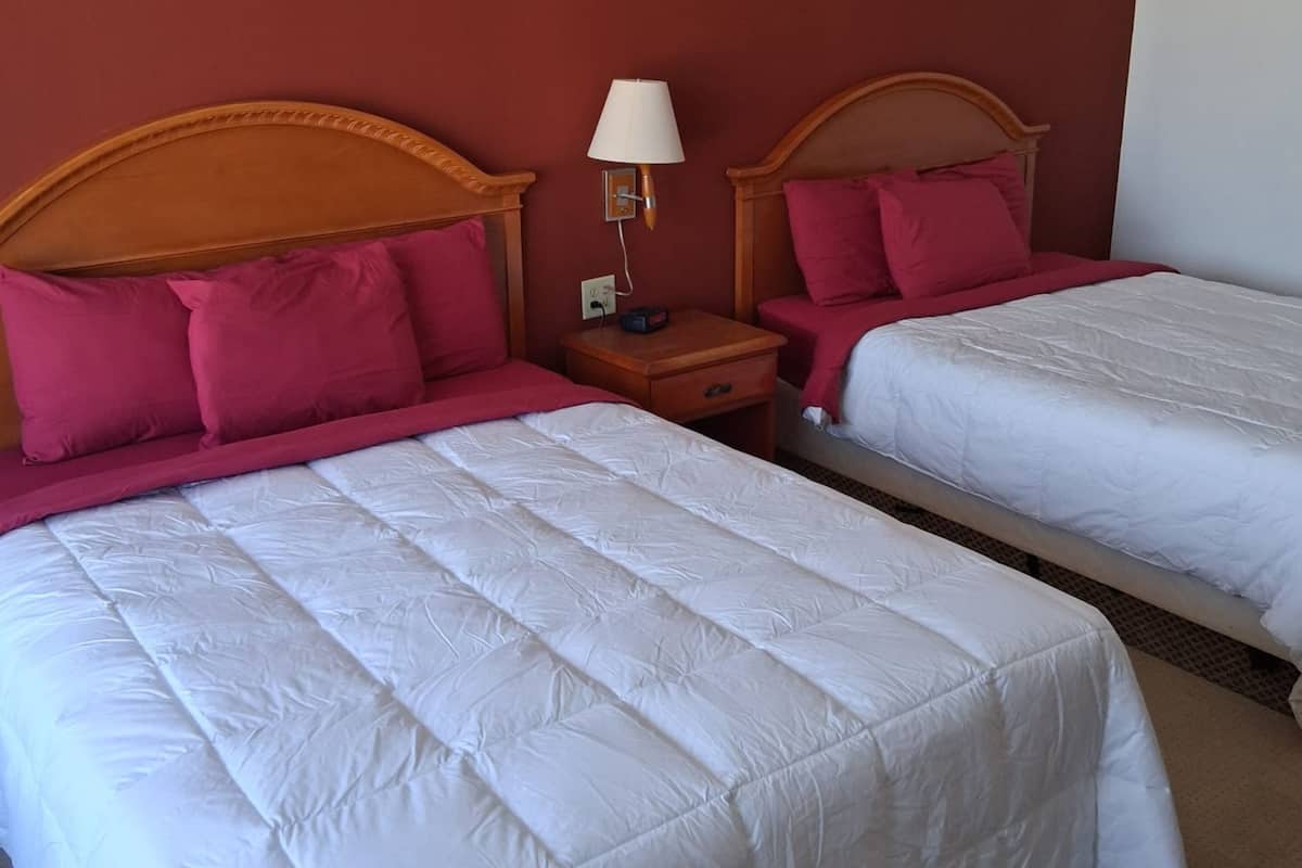 Two beds with wooden headboards, a nightstand with a lamp, and a red wall.