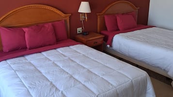Two beds with wooden headboards, a nightstand with a lamp, and a red wall.